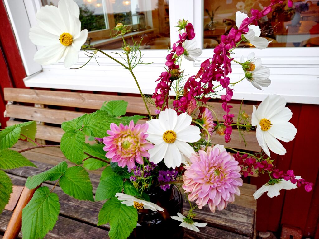 Bunter Blumenstrauß in einer Vase auf einer Holzbank, im Hintergrund ein Fenster; Blumen in den Farben Weiß, Rosa und Lila;